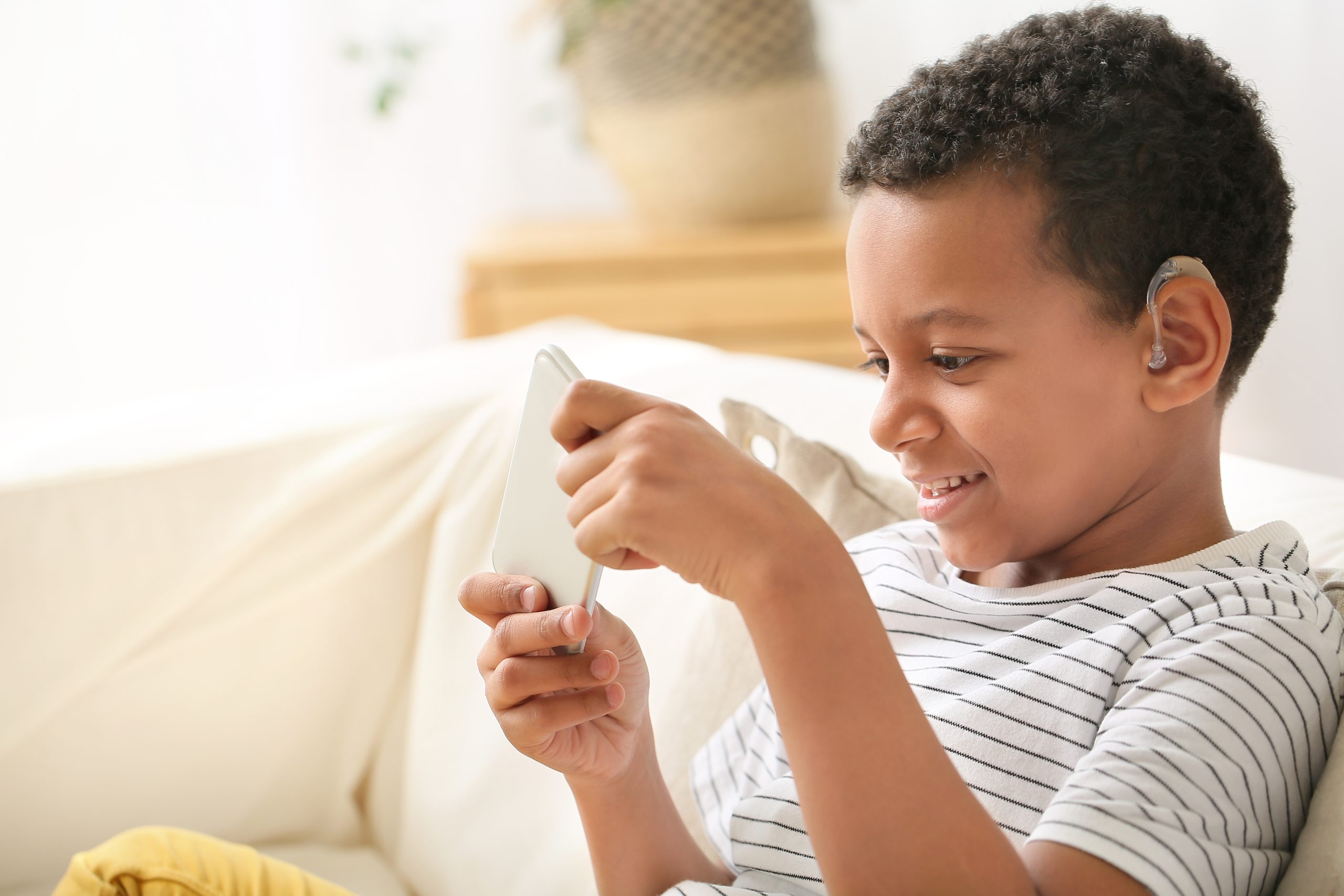 little african american boy with hearing aid using mobile phone at home