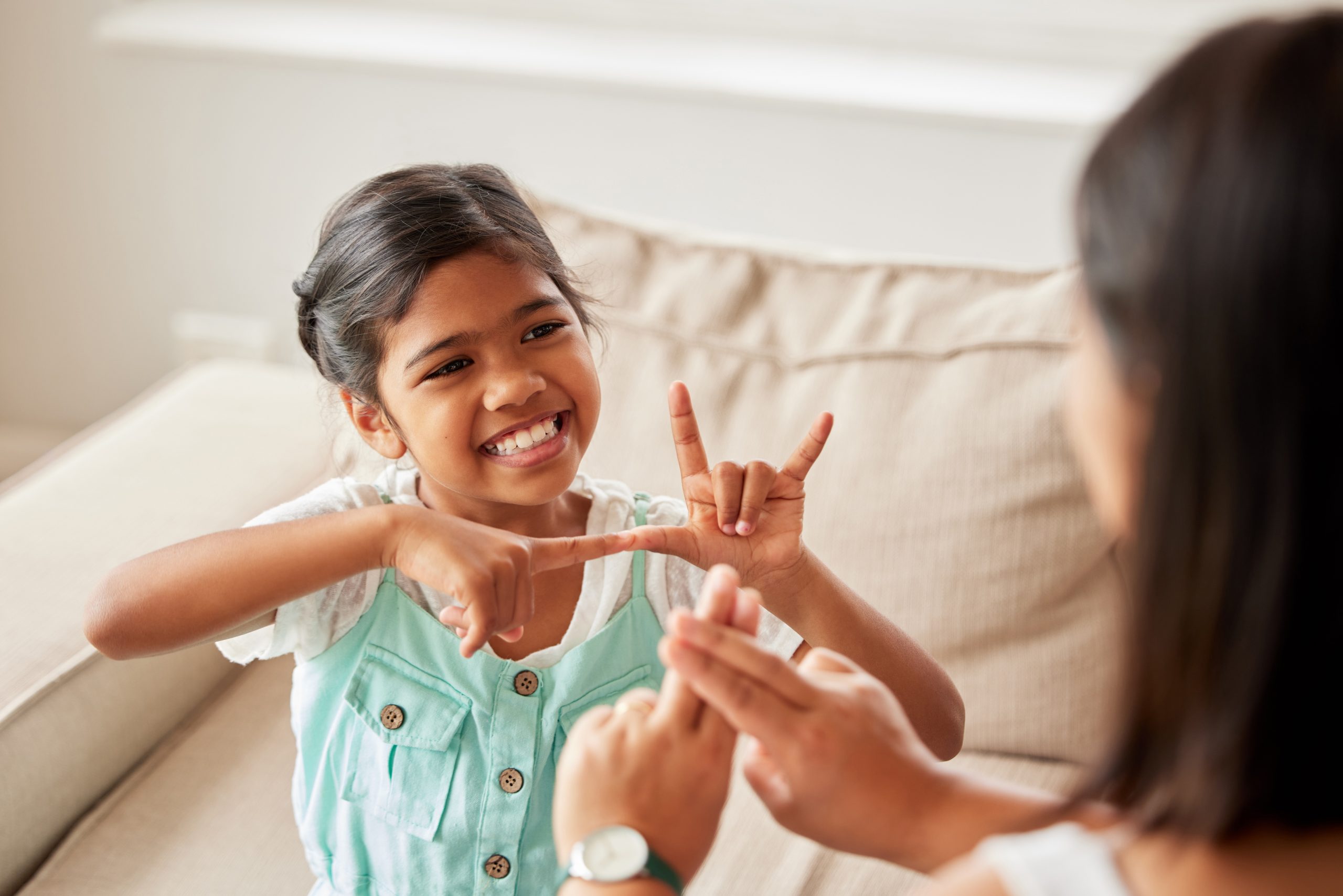sign language, communication and child with her mother in the living room of their family home. happy, smile and girl kid speaking with her hands to her deaf mom to communicate in their modern house.