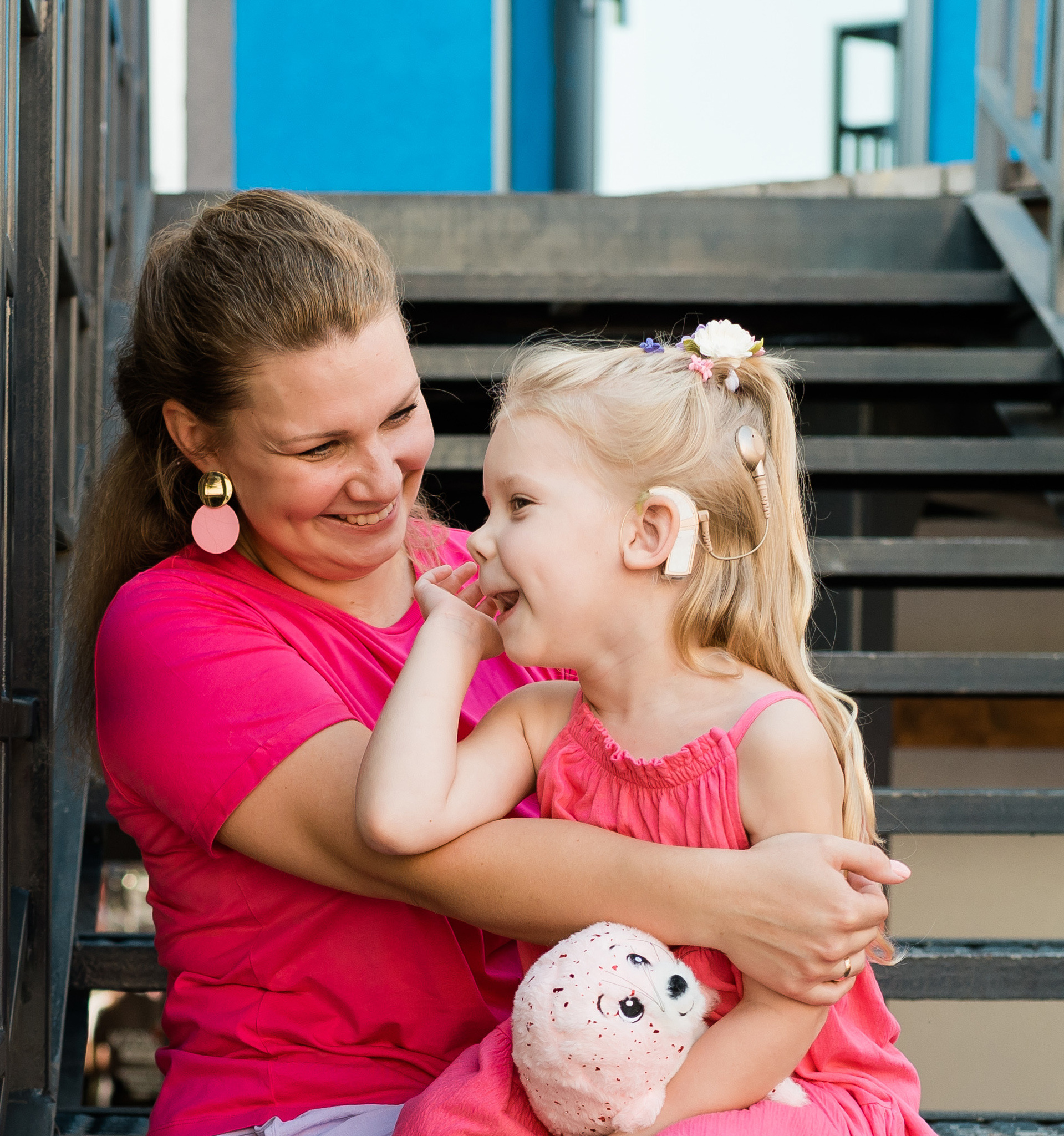blonde little girl with cochlear implant playing with her mother outdoor. hear impairment deaf and health concept. disability and inclusion. copy space